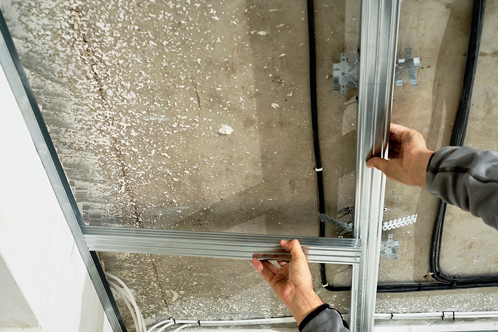 worker-adjusts-metal-profile-mounting-plasterboard-ceiling-frame-close-up-selective-focus-hands-specialist-industrial-renovation-renovation-min